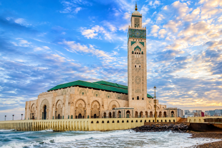 Hassan II Mosque in Casablanca, Morocco, standing beside the Atlantic Ocean under a dramatic blue and golden sky.